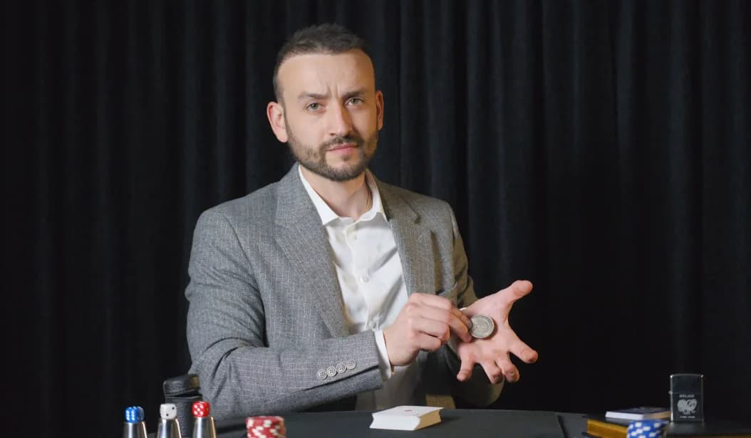 Tyson Dumas, magicien close-up — pièce en main, costume gris, en représentation