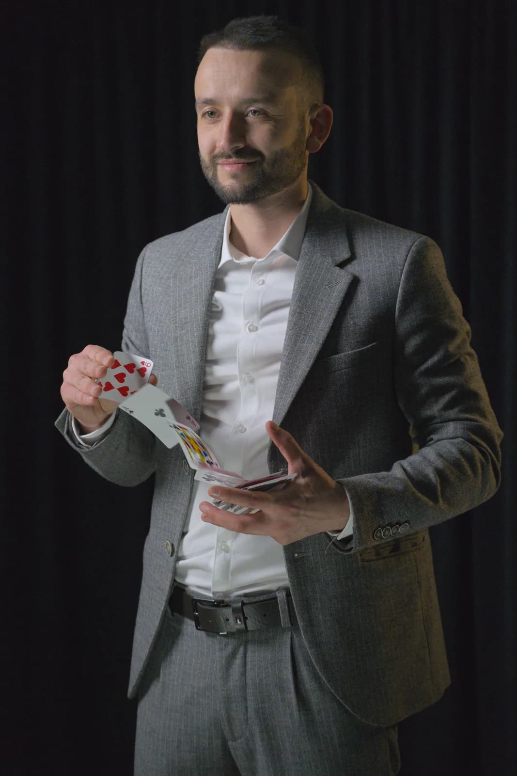 Tyson Dumas en costume trois-pièces gris debout en studio, manipulant un jeu de cartes pour un numéro de cartomagie