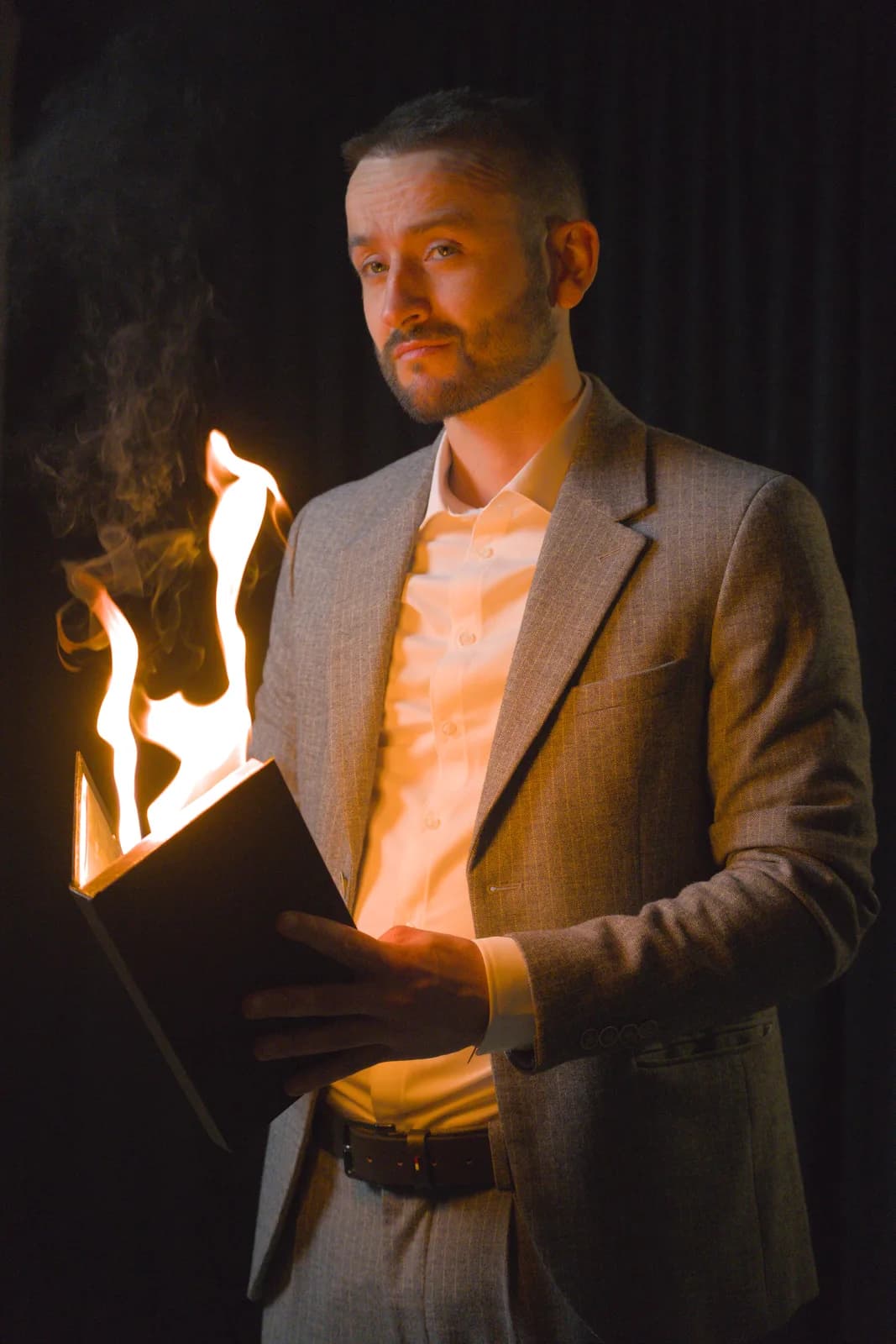 Tyson Dumas en costume beige avec un livre enflammé entre les mains, numéro de magie spectaculaire en studio